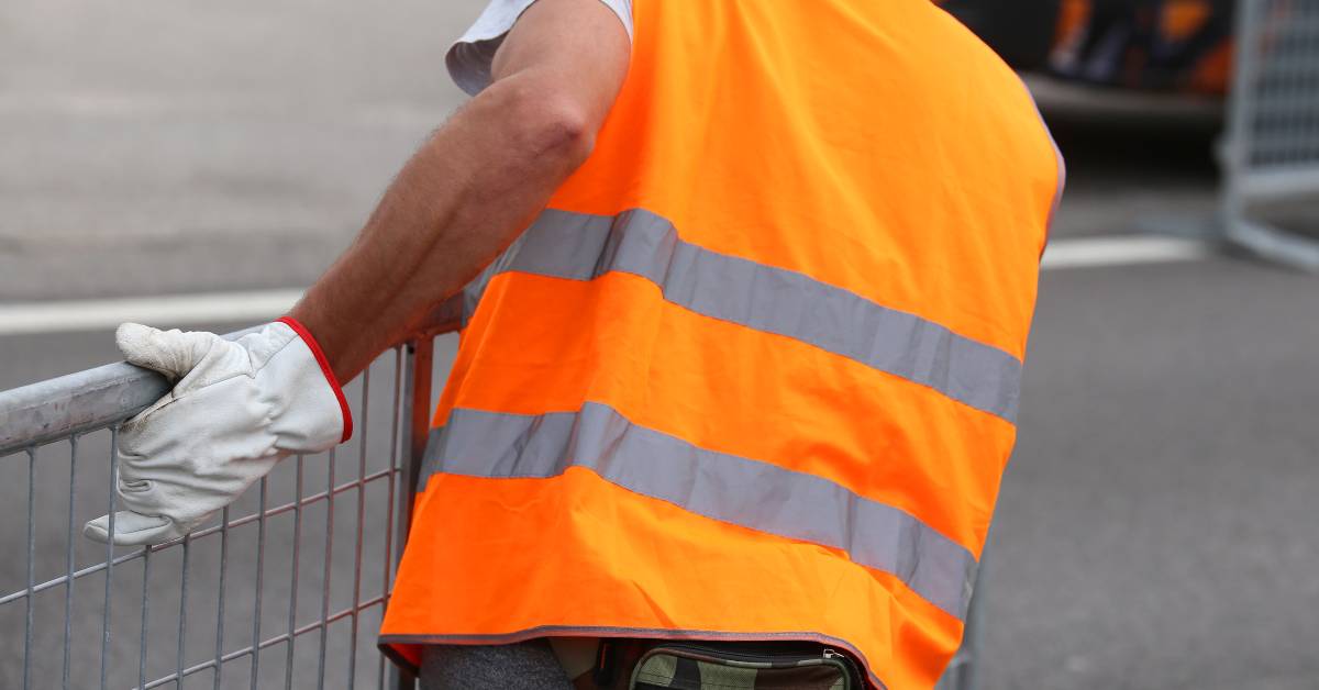 A fence rental provider securing a fence at an event. He is wearing a hazard vest and gloves to protect himself.